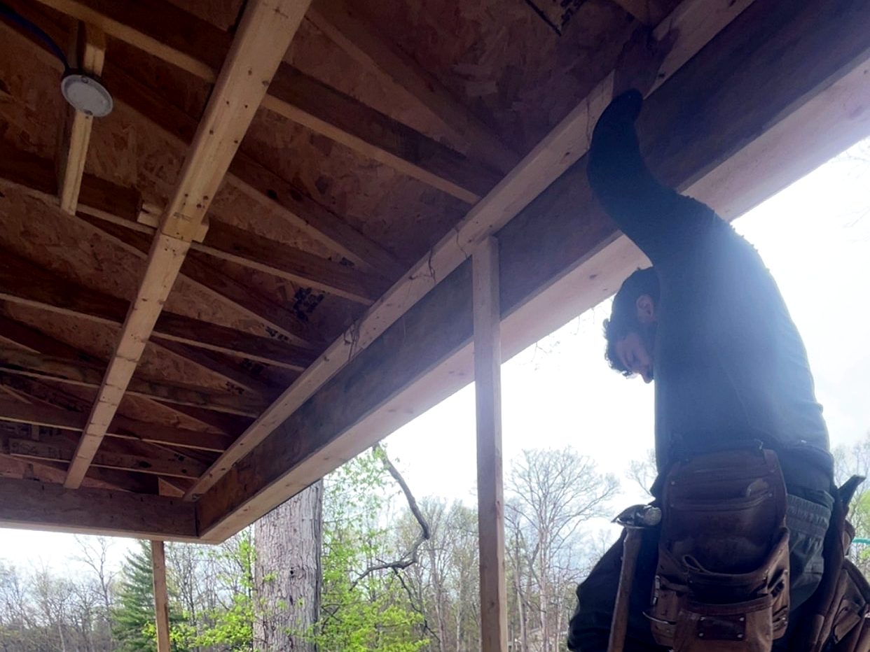 Crew member on a ladder finishing a porch ceiling on a service call