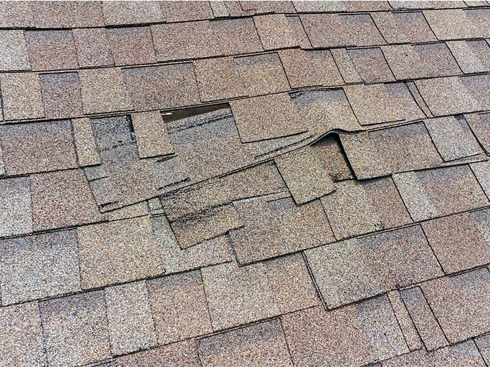 Close-up of wind-lifted and torn asphalt shingles on a damaged roof